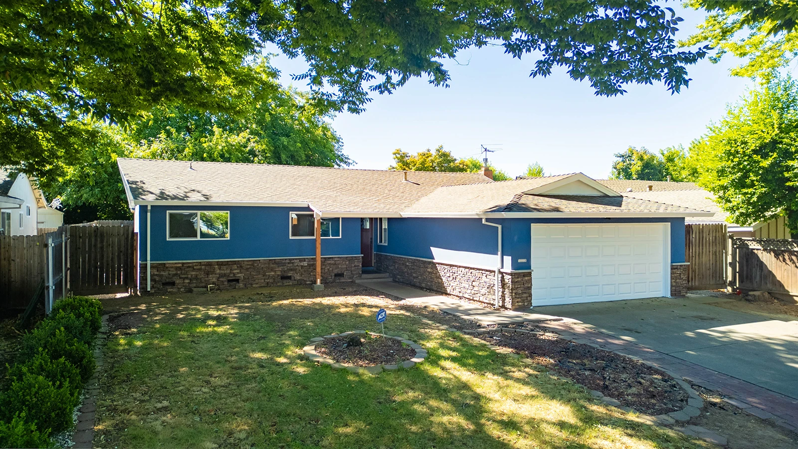 Single-story blue house with white two-car garage, stone accents, front lawn, and driveway