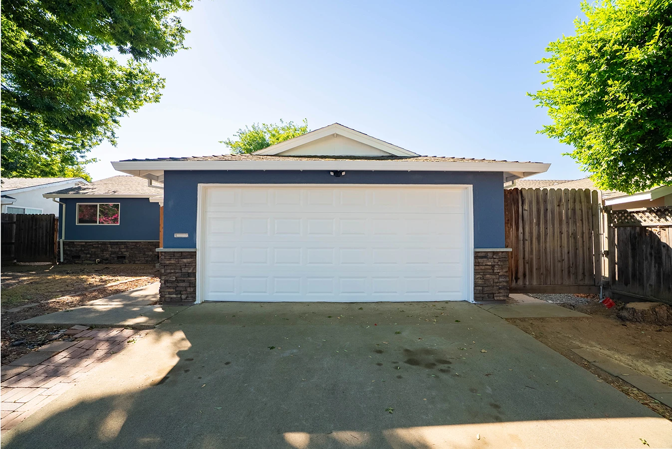 Front view of a blue house with a white double garage door, stone accents, and a concrete driveway
