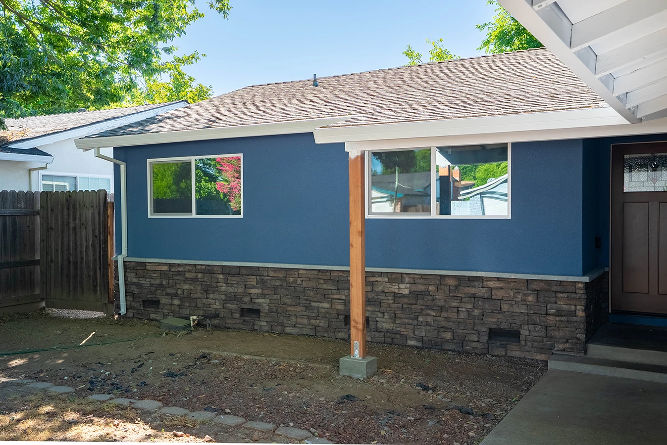 House exterior with blue stucco walls, stone veneer base, wood support post, and covered patio entryway