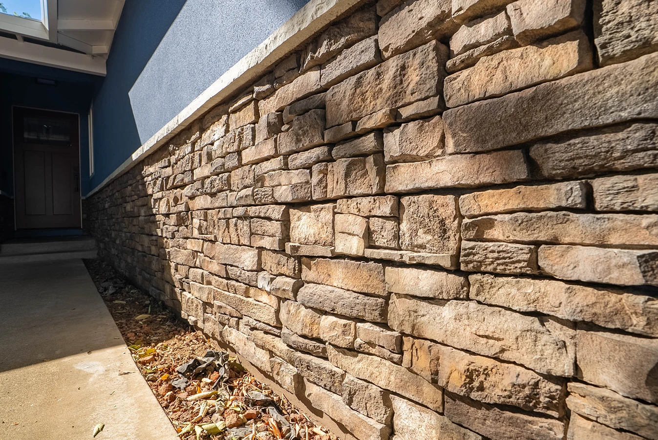 Stacked stone veneer wainscoting along a home's exterior wall beside the front entrance walkway