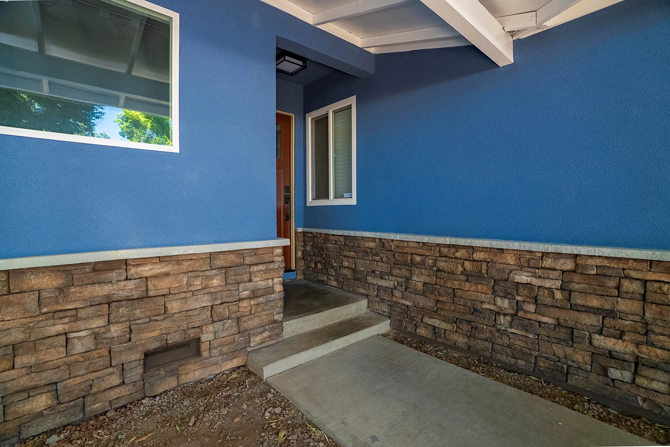 House entrance with blue stucco walls, stone veneer base, wood front door, and concrete steps leading to walkway