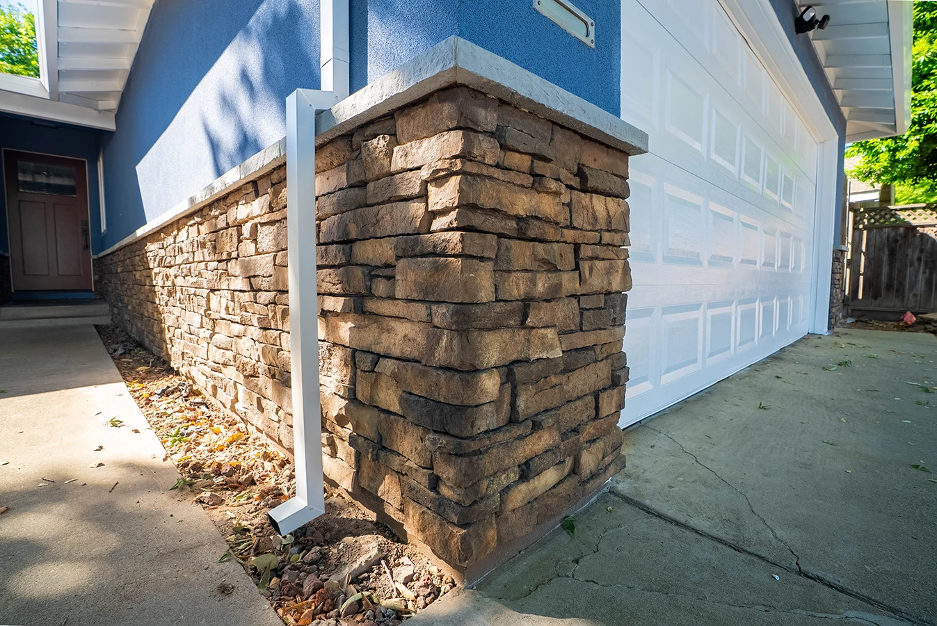 House exterior with stacked stone veneer base, blue siding, and white garage door