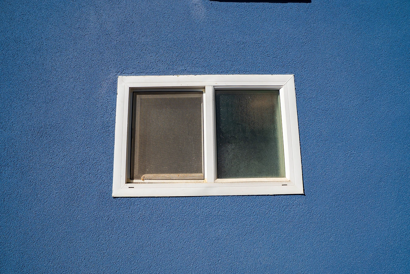White-framed window with a screen panel, set in a textured blue stucco wall