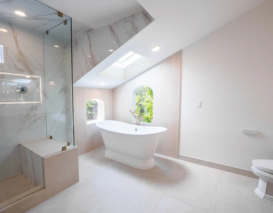 Bathroom with a freestanding soaking tub, skylight, marble-tiled walk-in shower, arched windows, and wood vanity