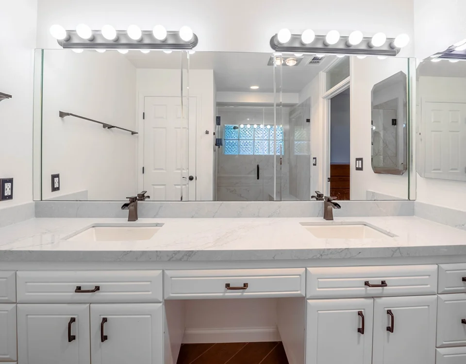 White double-sink bathroom vanity with marble countertop, lit mirrors, and dark bronze hardware