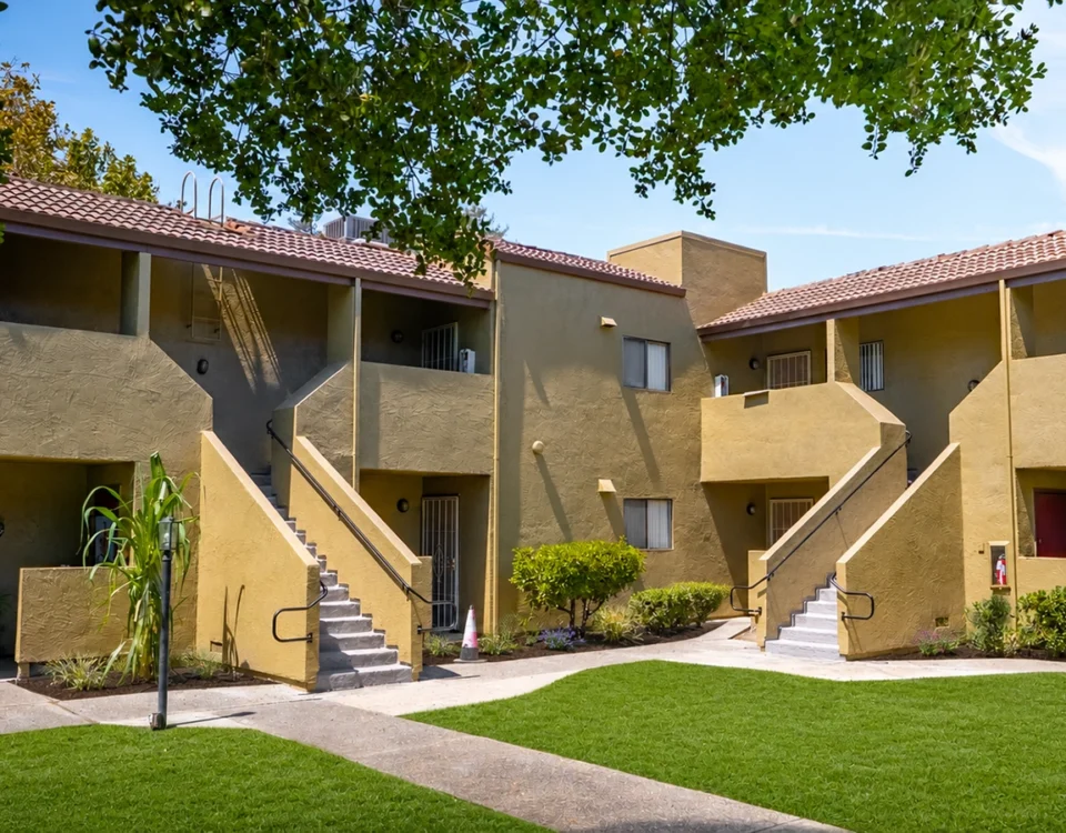 Two-story tan apartment buildings with exterior staircases, landscaped courtyard, and tile roofs