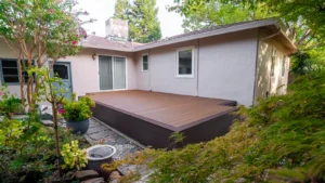 Backyard composite deck attached to a house, surrounded by lush landscaping and a stone pathway