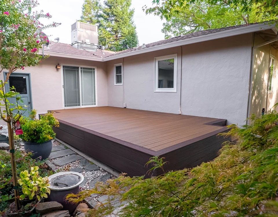 Backyard composite deck attached to a house, surrounded by lush landscaping and a stone pathway